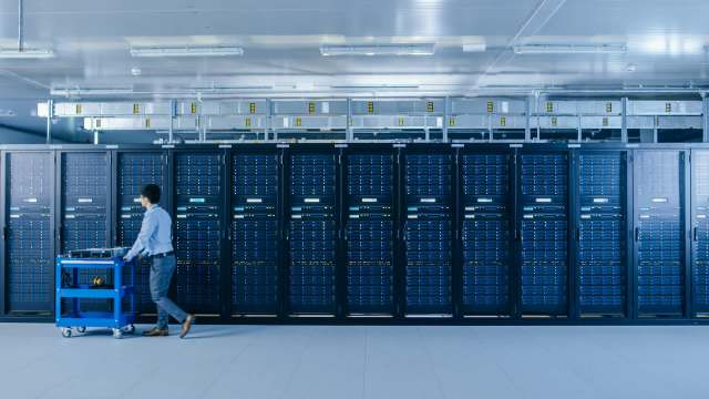 A technician pushes a blue cart alongside rows of server racks in a modern data center.
