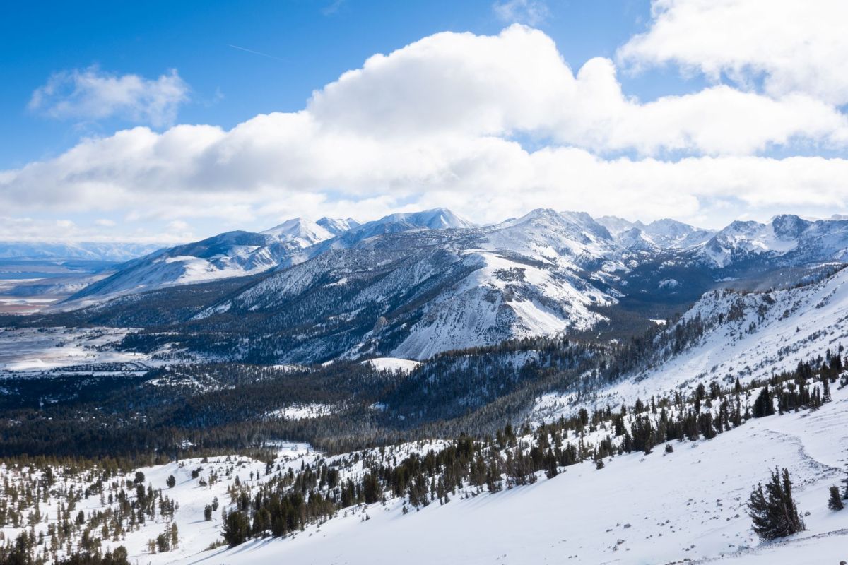 A panoramic view of snow-covered mountains under a bright blue sky with scattered clouds.