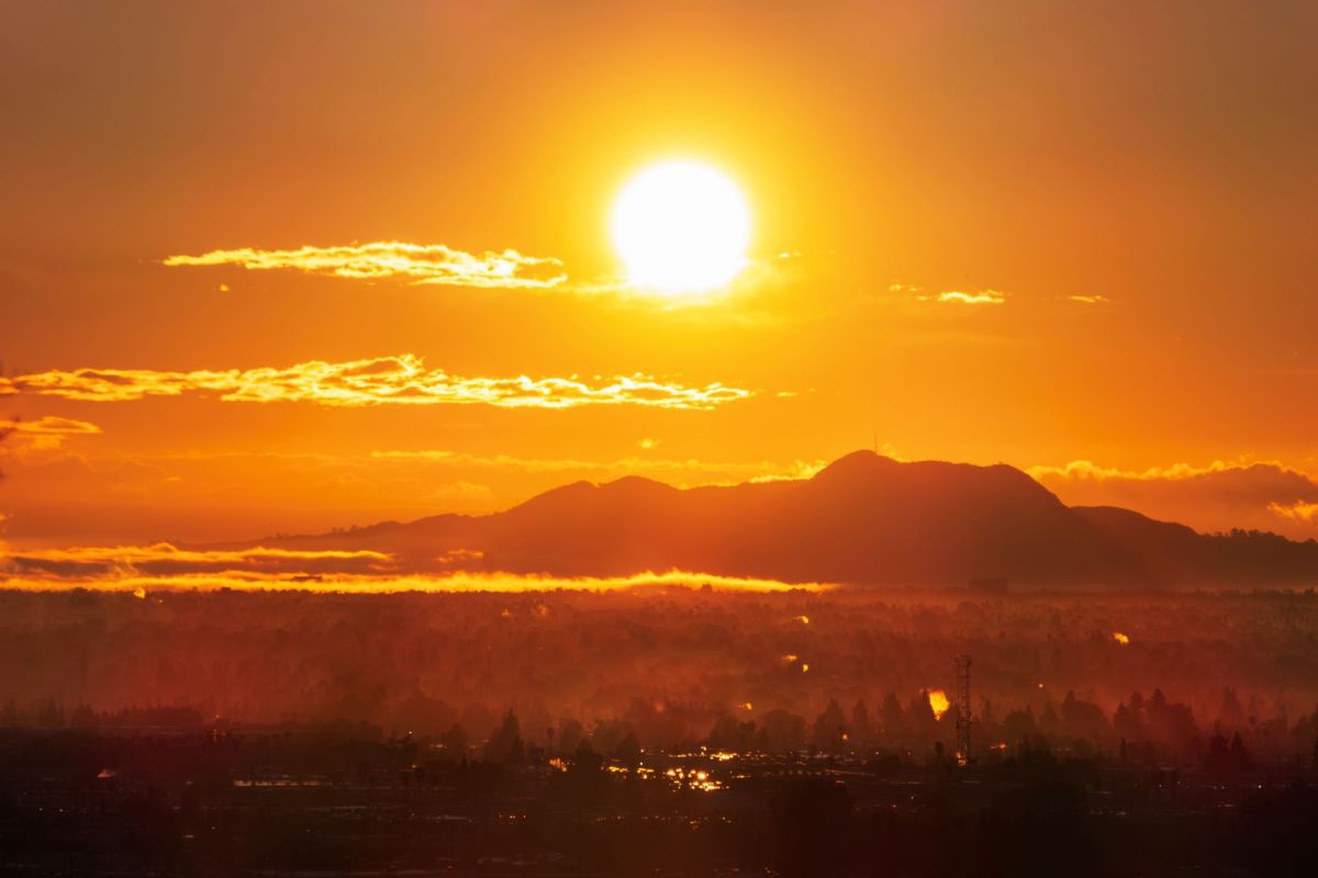 A vibrant sunset casts orange and yellow hues over silhouetted mountains and a misty landscape.