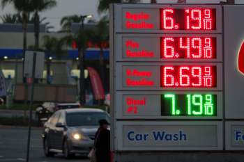 A gas station sign displaying fuel prices for regular, plus, V-Power gasoline, and diesel at dusk.