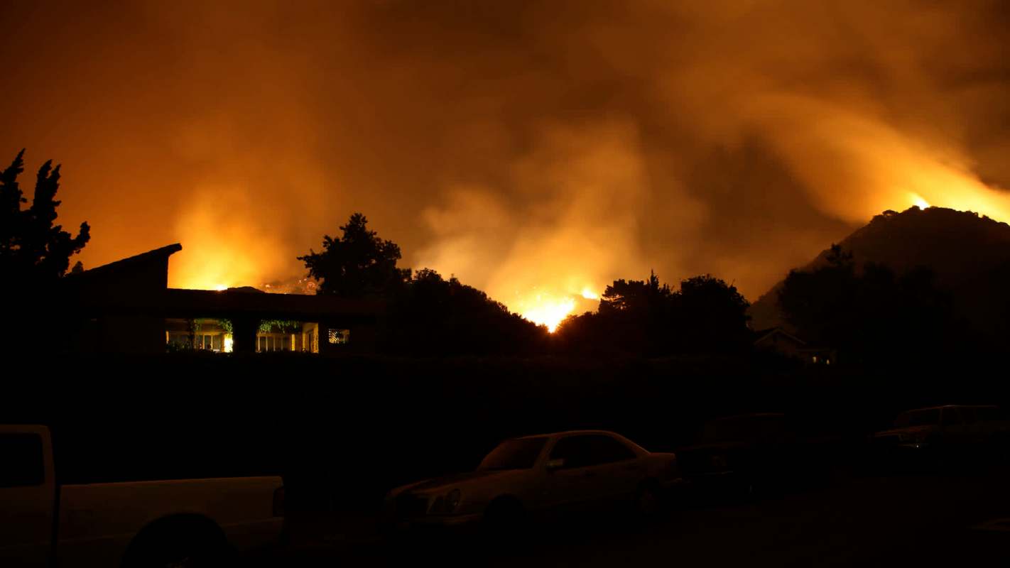 A dramatic night scene of a wildfire glowing against a smoky orange sky.