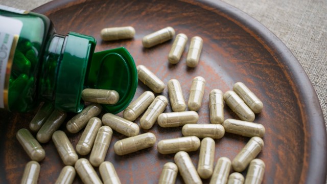 A green bottle tipped over, spilling numerous herbal capsules onto a wooden plate.