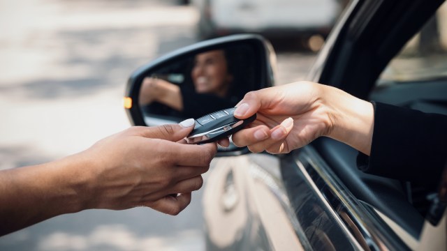 A person hands over a car key to another individual from a vehicle's window.