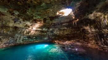 A dramatic underground cave features crystal-clear water and a sunlight opening above.