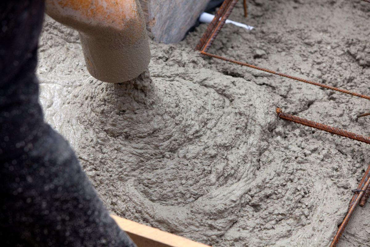 Fresh concrete being poured into a form with exposed rebar, showcasing a textured surface.