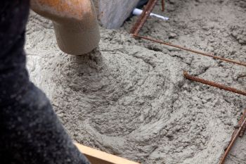 Fresh concrete being poured into a form with exposed rebar, showcasing a textured surface.