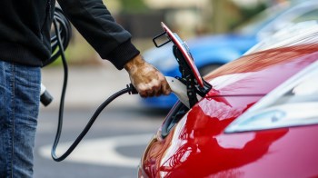 A person is plugging an electric charging cable into the port of a red electric vehicle.