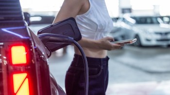A person holds a smartphone while charging an electric vehicle in a parking garage.