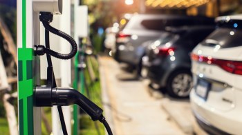 An electric vehicle charging station with cars parked in the background at night.