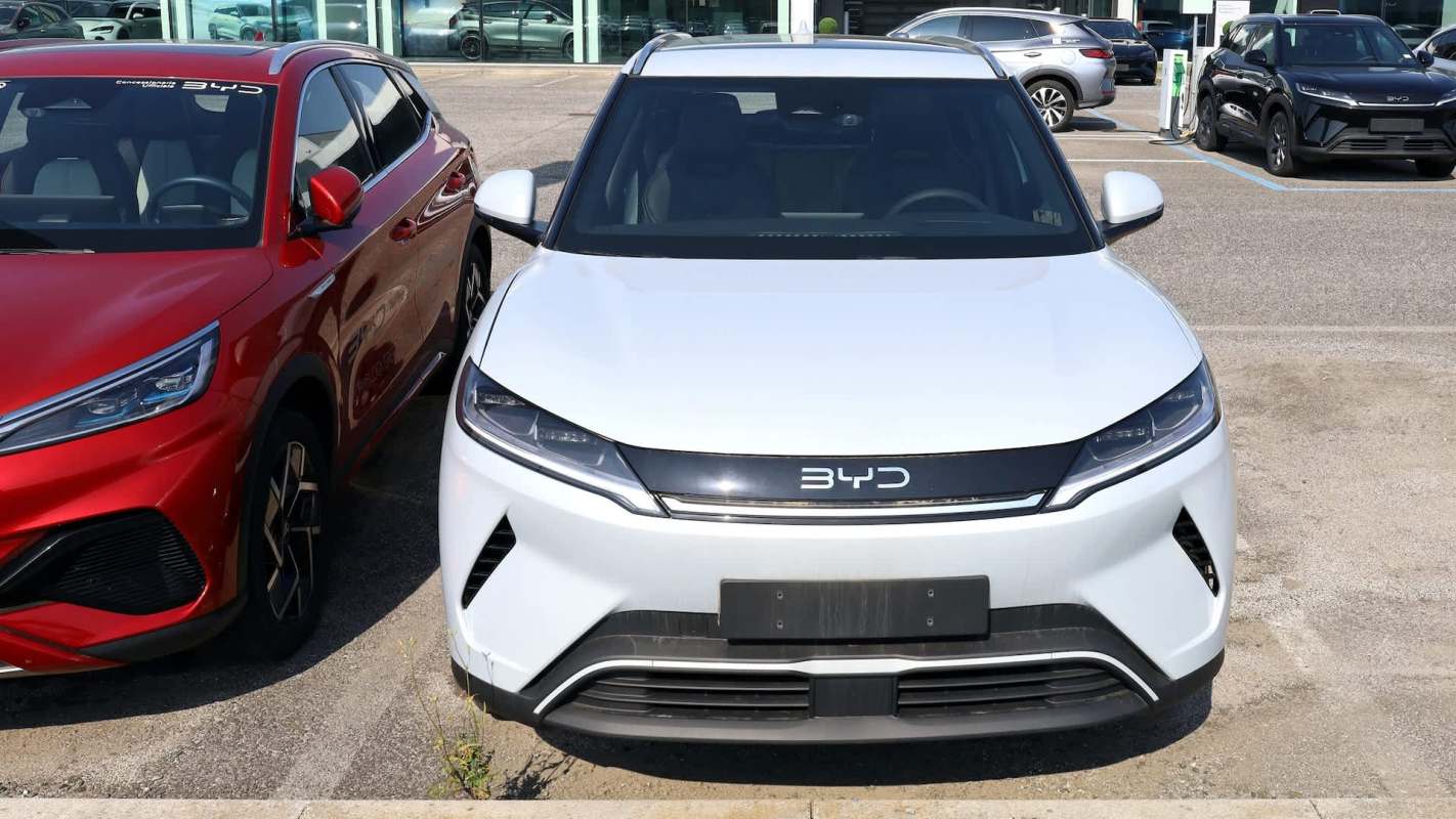 A white BYD electric vehicle parked next to a red SUV in a car dealership lot.
