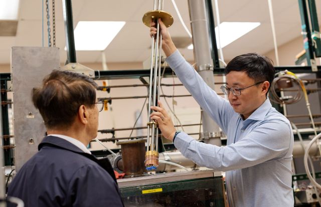 A researcher demonstrates a scientific apparatus to a colleague in a laboratory setting.