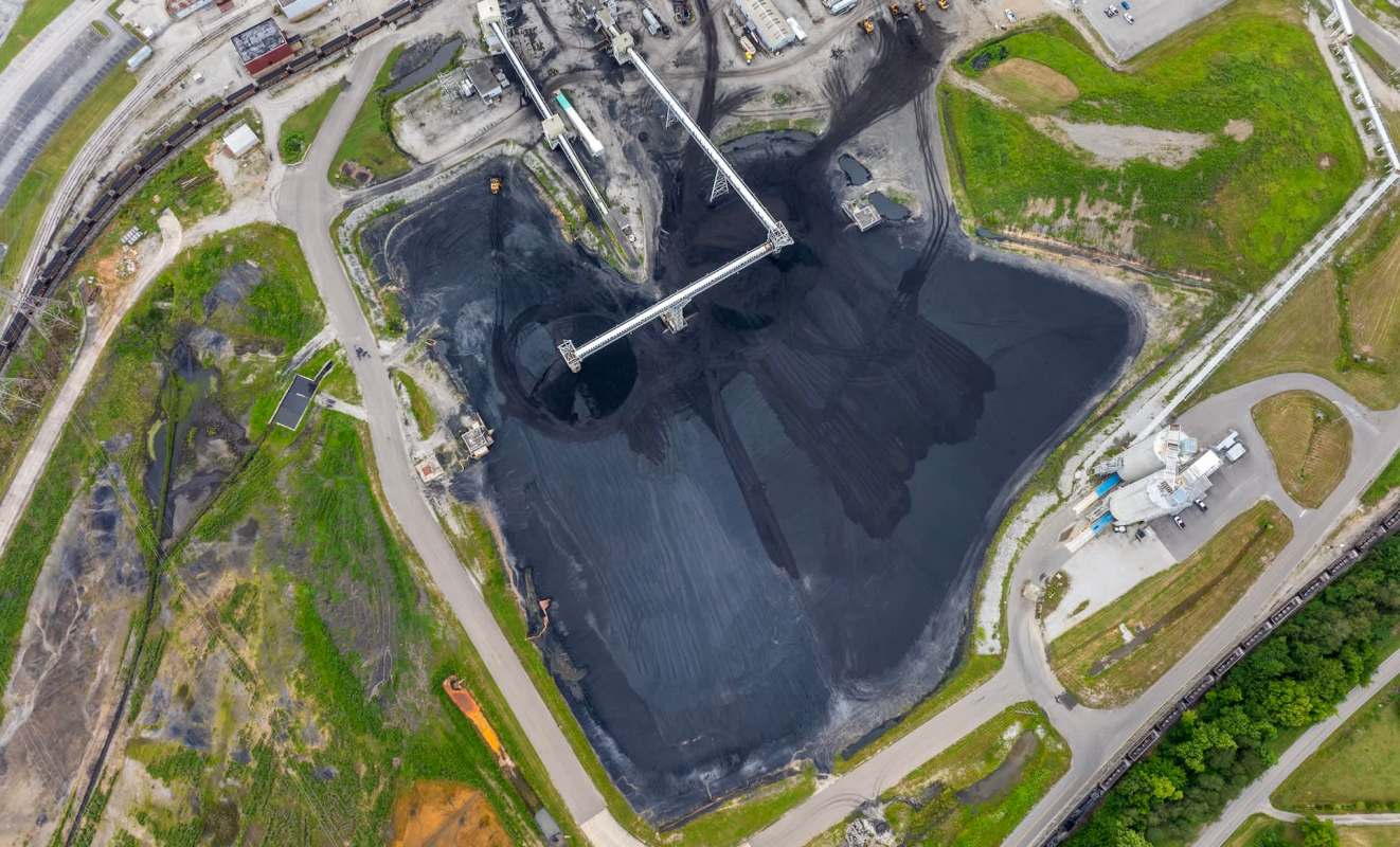 An aerial view of a coal storage area with a conveyor system and surrounding greenery.