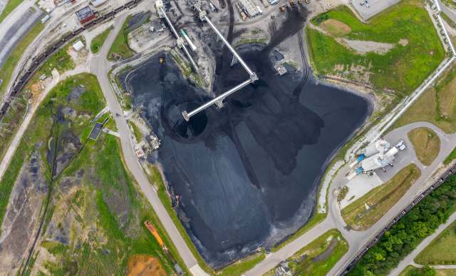 An aerial view of a coal storage area with a conveyor system and surrounding greenery.