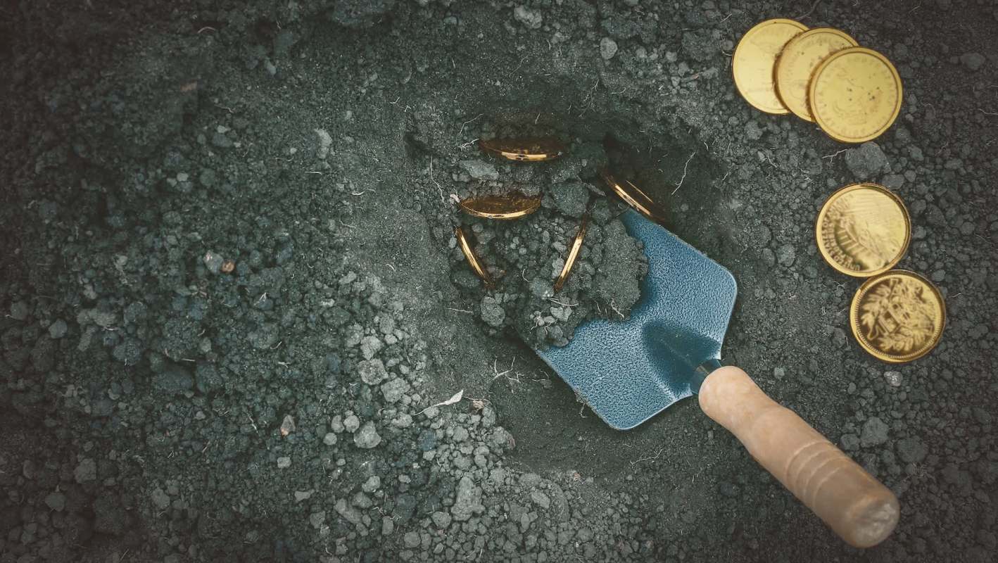 A trowel digs into the earth and reveals shiny gold coins.