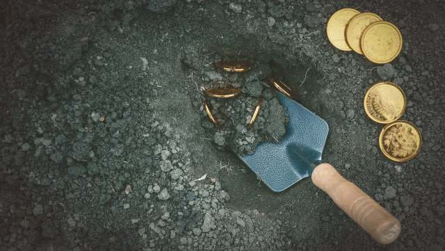 A trowel digs into the earth and reveals shiny gold coins.
