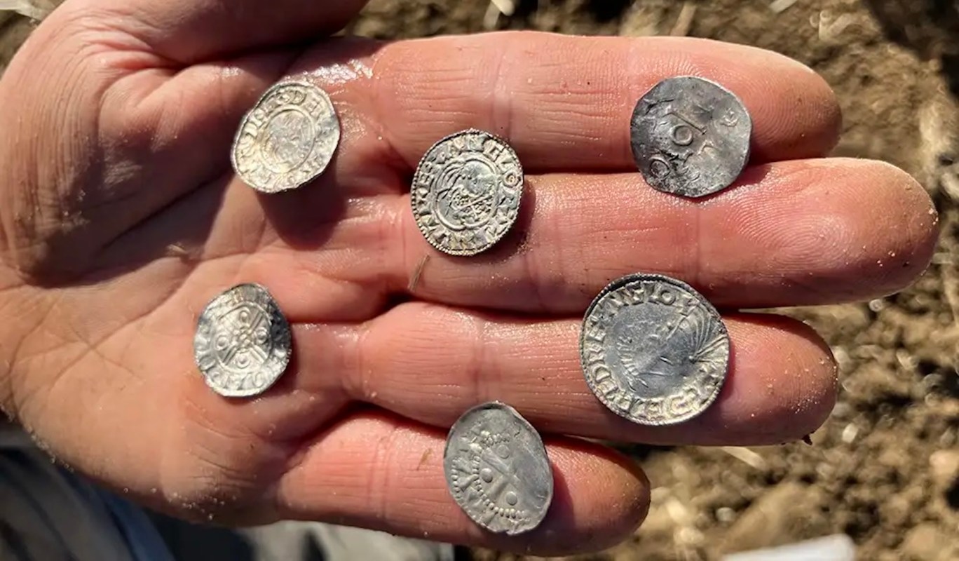 A hand holding six ancient silver coins, some displaying intricate designs and inscriptions.