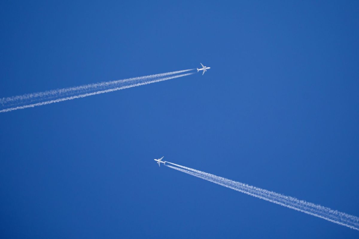 Two airplanes flying in a clear blue sky, leaving contrasting white contrails behind them.