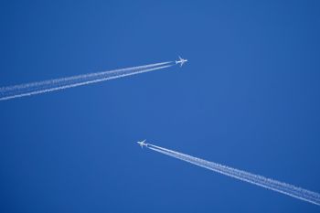 Two airplanes flying in a clear blue sky, leaving contrasting white contrails behind them.