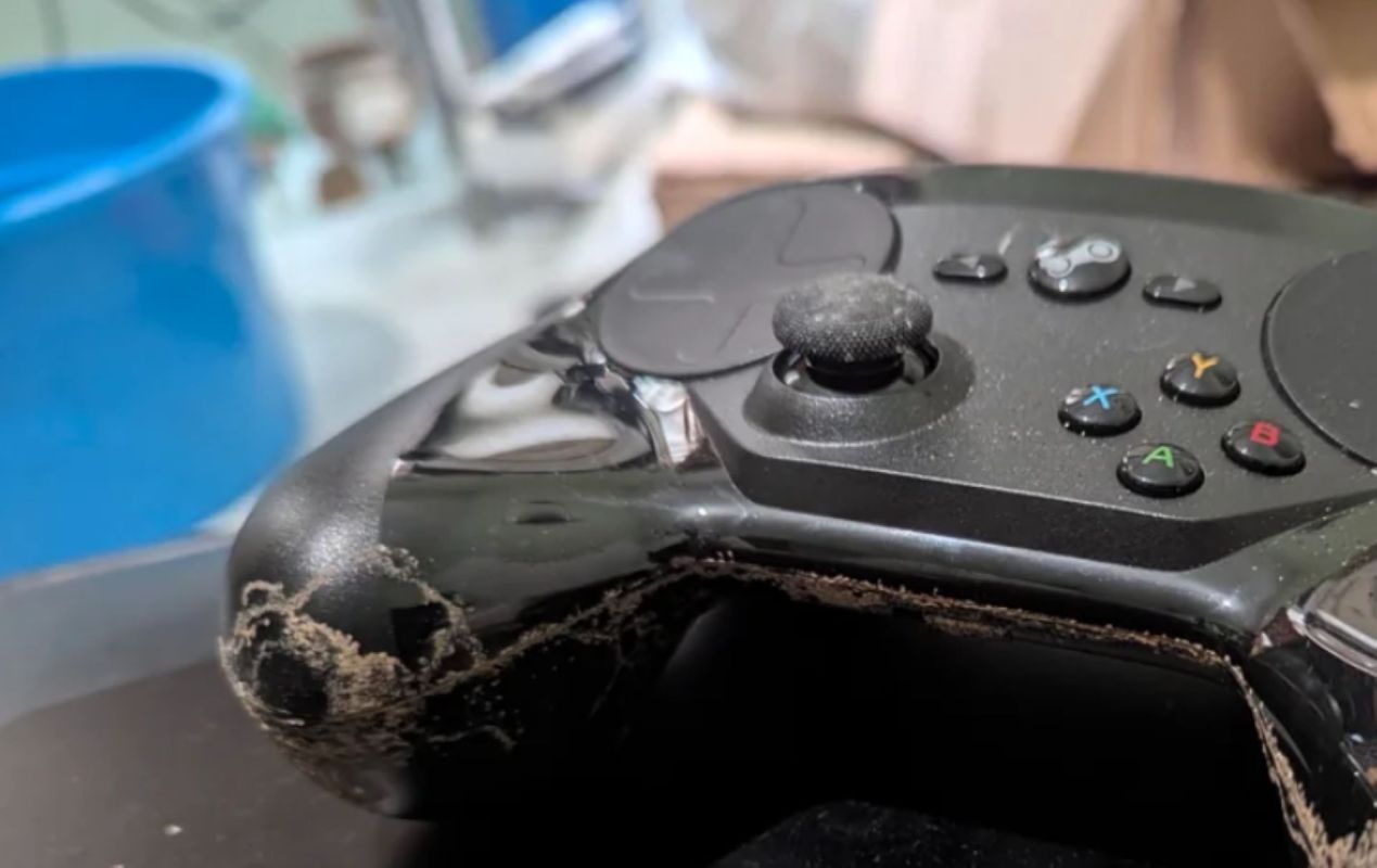 A close-up of a worn gaming controller with dust and a visible scratch along the edge.