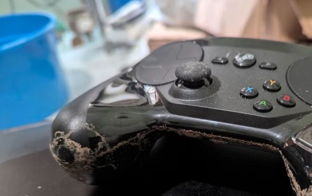 A close-up of a worn gaming controller with dust and a visible scratch along the edge.