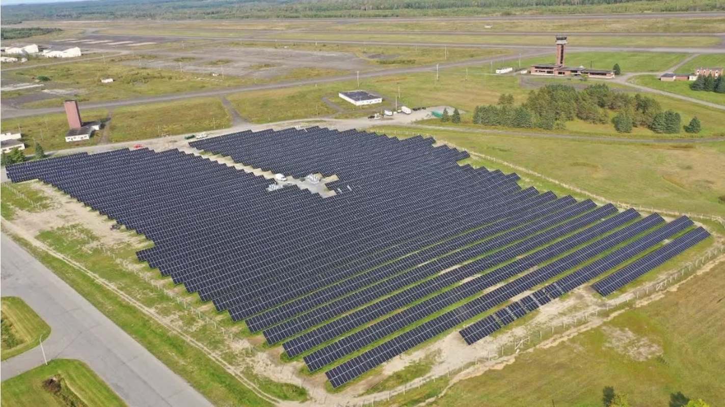An aerial view of a large solar panel field next to an airstrip and a control tower.