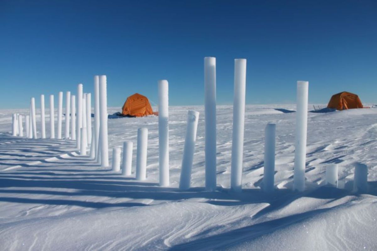 Snow-covered landscape with vertical ice cores and an orange tent against a clear blue sky.