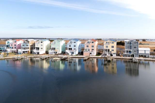 Colorful waterfront houses with docks reflecting in the water on a clear day.
