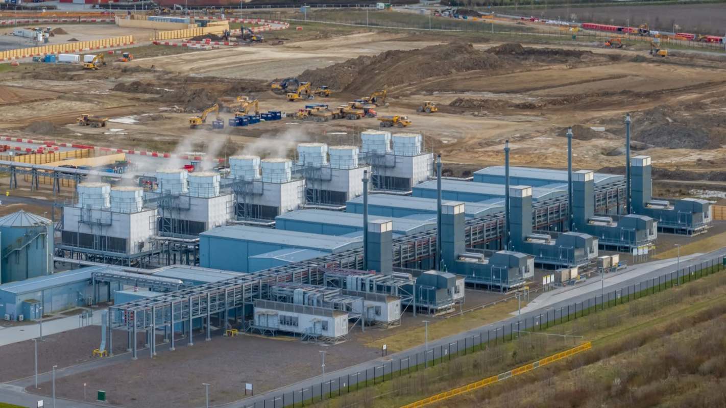 An industrial site for a data center featuring large cooling towers and machinery with a construction area in the background.