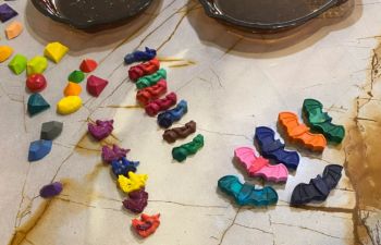 Colorful crayon pieces shaped like gems and bats arranged on a marble tabletop.