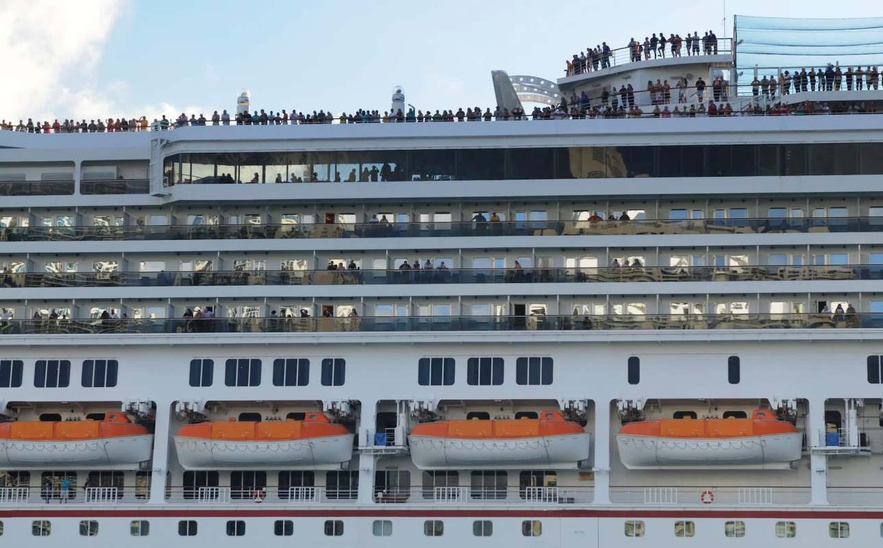 A cruise ship deck filled with passengers , with lifeboats visible below.