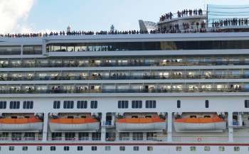 A cruise ship deck filled with passengers , with lifeboats visible below.