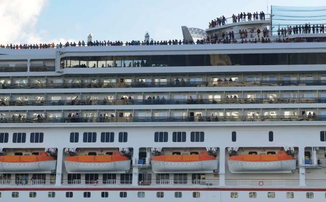 A cruise ship deck filled with passengers , with lifeboats visible below.