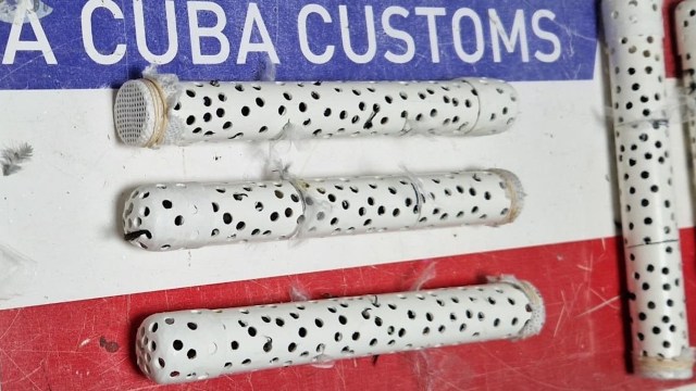 A series of white tubes with black dots resting on a colorful surface marked with "CUBA CUSTOMS."