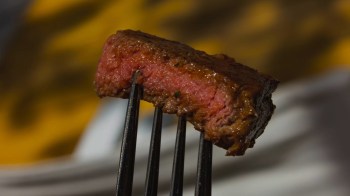 A close-up of a medium-rare steak piece held by a fork, showcasing its pink center.