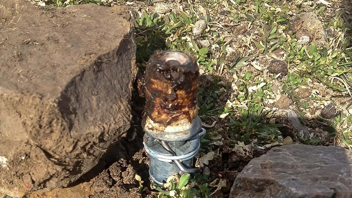 A rusty metal pipe-like device surrounded by dirt and small rocks.