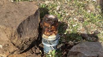 A rusty metal pipe-like device surrounded by dirt and small rocks.