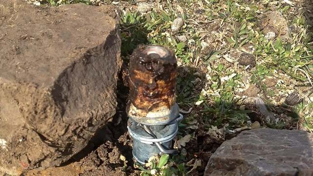 A rusty metal pipe-like device surrounded by dirt and small rocks.