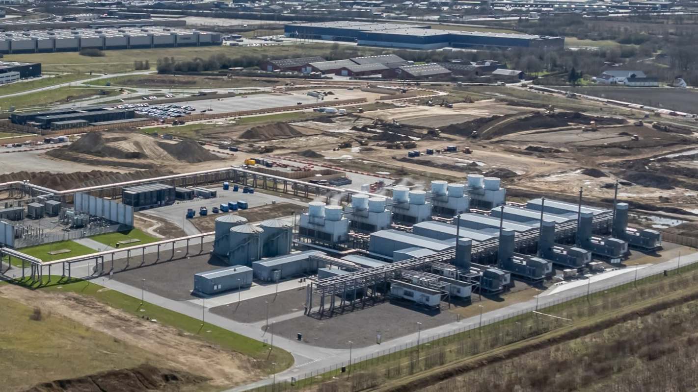 An industrial facility with large structures and tanks under development, surrounded by construction and parking areas.