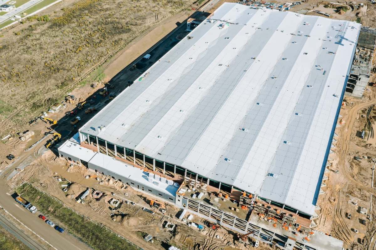 Aerial view of a large industrial building under construction with various machinery and materials around it.