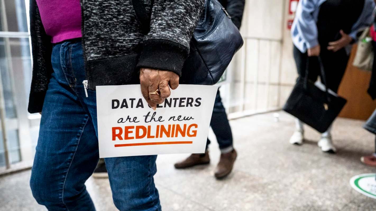 A person holds a sign reading "DATA CENTERS are the new REDLINING" while walking through a public area.