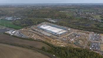 An aerial view of a large construction site with heavy machinery and vehicles surrounded by green fields and trees.