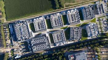 Aerial view of a complex of data centers featuring modern buildings and solar panels, surrounded by green fields and roads.
