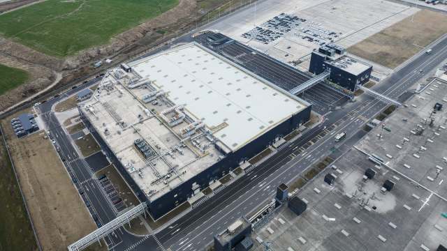 An aerial view of a large industrial facility with parking areas and surrounding green fields.