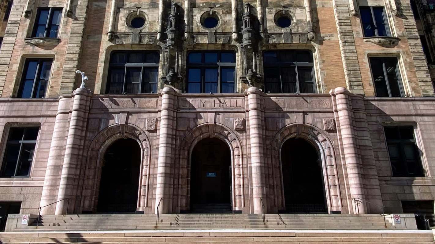 The grand entrance of a historical city hall building features ornate architecture and three arched doorways.