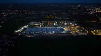 An aerial view of a brightly lit industrial area at night, surrounded by fields and residential areas.