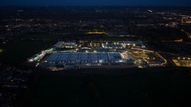 An aerial view of a brightly lit industrial area at night, surrounded by fields and residential areas.