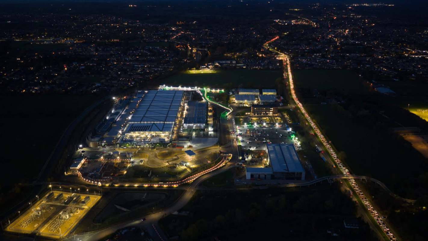 An aerial view of a brightly lit industrial area at night, with traffic flowing along a winding road.