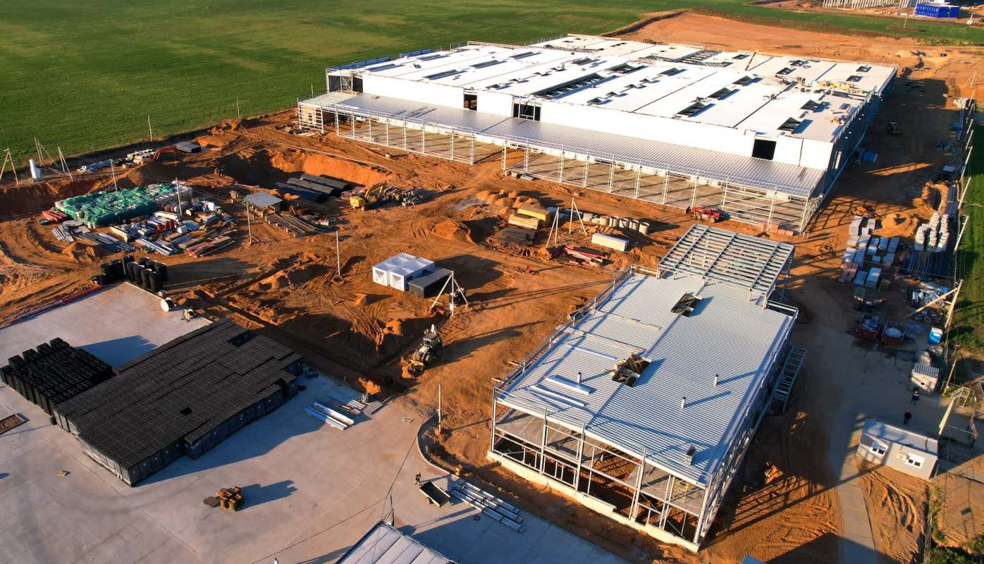 An aerial view of a construction site with two buildings and various equipment and materials on the ground.