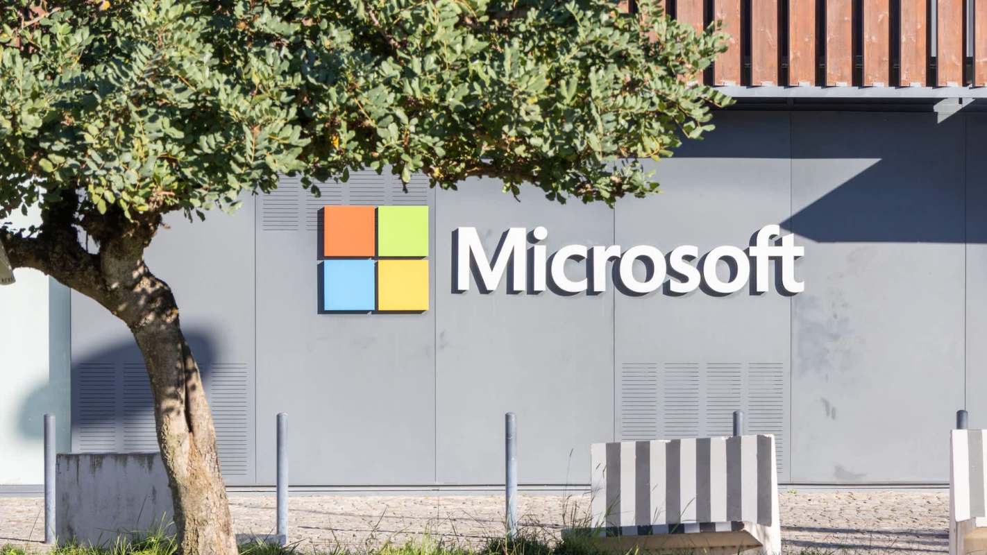 A Microsoft logo displayed on a building's exterior, with a tree and benches in the foreground.