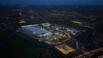 An aerial view of a well-lit data center near a city at dusk, featuring warehouses and sports fields.